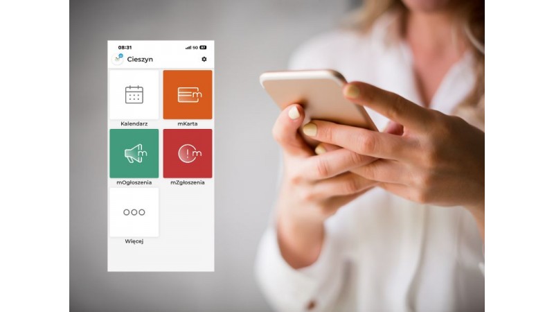 Kobieta trzyma smartfon; obok widoczny ekran aplikacji „Cieszyn” z dużymi, kolorowymi kafelkami: Kalendarz, mKarta, mOgłoszenia, mZgłoszenia i Więcej.